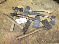 Lot of 6 hand axes and hatchets arranged on wooden surface, showing variety in sizes, handle materials, and blade shapes.