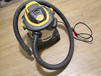 Shop-Vac wet/dry vacuum cleaner on wood floor with attached hose and power cord visible.