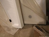Two white textured shower bases wrapped in bubble wrap leaned against wall