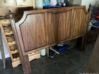 Front view of one wooden queen headboard showing paneled wood design and legs.