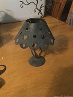 Metal tealight holder with heart cutouts on scalloped edge, grey colored, on wooden table.