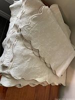 Photo showing folded white king size bedspread and two matching pillow cases with floral embossed design and scalloped edges.