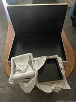 Large wooden rectangular box open showing black interior and multiple smaller trays wrapped in paper.