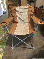 Front view of brown and tan large fold-up camping chair with steel frame and two cup holders on armrests.