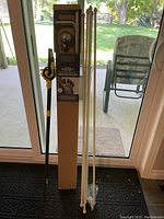 View showing black metal boxed curtain rod with spherical finial and five cream-colored curtain rods with pointed decorative finials.