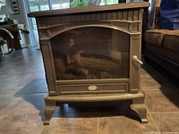 Front view of black Dimplex electric fireplace with faux log and glass front, showing the full unit with curved top and legs.