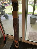 Photo of Allen + Roth double drapery rod set in original packaging standing upright indoors near sliding glass doors.