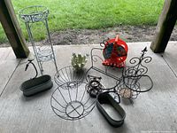 Overview of metal garden planters, plant stand, hose reel, decorative wire items on patio floor