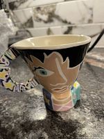 Hand painted tea cup showing an abstract face design on ceramic with glazed finish