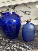 Photo showing both large shiny cobalt blue glass vase and smaller matte cobalt blue bottle with cork lid on granite countertop