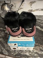 Pair of Laurentian ladies moccasins displayed on top of original blue and white Eugene Cloutier Inc. box, showing front upper with black rabbit fur trim and beading detail.