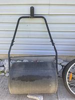 Front view of the used lawn roller showing black cylindrical roller and metal frame with handle.