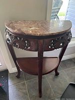 Full view of the mahogany half moon entry table with marble top, showing its shape and wood carvings.