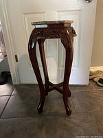 Side photo showing the elegant curved legs and carved wood apron beneath the marble top of the mahogany plant stand.