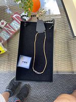 Photo showing a necklace with black beads and gold-tone chain with a bead cluster, a small ring with two round ornaments, and a gold-tone bangle with a decorative charm arranged on a black tray.