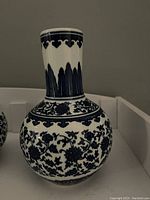 Side view of one ceramic vase showing blue floral and leaf designs on white background with narrow neck and round body.