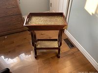Front angle view of the table showing dark wood frame and brass inset trays on top and lower shelf, placed on wooden floor near vent and wall.