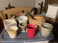 Multiple plant pots and holders of assorted sizes, colors, and materials on a blue surface.