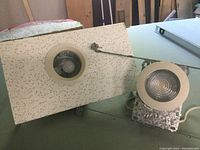 Close-up of one pot light installed in drop ceiling tile showing round rim, light bulb, and mounting hardware.