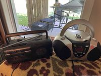 Photo showing two radios: one Sony radio cassette player and one silver and black CD boombox radio on a patterned surface.