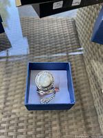 Silver-tone ring with large opal-like centerpiece surrounded by clear stones in a blue box