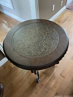Top view of round side table showing intricate light-colored floral and leaf pattern on dark tabletop surface.