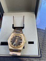 Seiko Sports 100 quartz watch in original display box showing gold-tone stainless steel bracelet and black dial with day-date window.