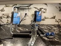 Photo of three foam-padded storage hangers with blue caps on ends, some with tags attached indicating new condition, on a countertop with marble-style backsplash.