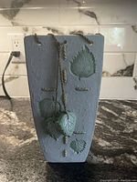 Light green ceramic vase with raised leaf designs and twine hanging decoration.