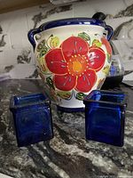 Front view of the ceramic flower planter with bright floral decoration and two cobalt blue glass holders beside it.
