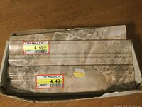 Box containing new wall tiles, two visible tiles packaged with price stickers