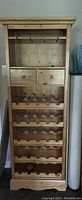 Full frontal view of the pine wine cabinet showing the 25-bottle wine rack, two drawers, and upper storage shelf with glass holders.
