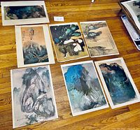 Seven unframed art prints laid out on a wood floor showing Chinese styled paintings including landscapes and floral scenes.