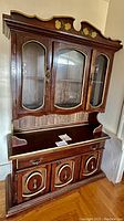 Front view of Bassett wooden hutch showing glass display cabinet with three curved glass panels, ornate trim and top carvings, drawers, and lower storage cabinet with three doors