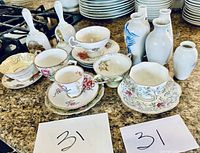Overview of all items including tea cups, saucers, bells, and vases on counter