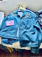 Photo showing a blue denim jacket decorated with metal studs placed on top of other garments hung on hangers.