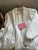 White women's jacket with shawl collar, hung on pink hanger, with a pink note showing size 12 and brand Giorgio Sant'Angelo