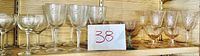Full set of 12 colored and clear glasses on wood shelf showing grouping and variety.