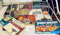 Collection of board games, puzzles, A-10 Thunderbolt II plastic model airplane kit, and painting shown stacked on a white surface.