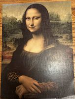 Printed reproduction of Mona Lisa painting showing the iconic portrait with finely detailed hands and facial expression, printed on textured paper.