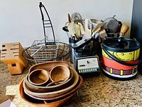 Photo of the lot showing kitchen utensils in containers, blender base, wooden bowls, metal baskets, and colorful ice bucket on counter.