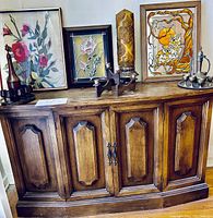 Full view of mid-century wooden cabinet with three framed artworks and candle holder sets on top