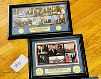 Photo of two rectangular black frames on wooden floor, each containing multiple images of Barack Obama, commemorative gold seals, and engraved plaques honoring Barack Obama.