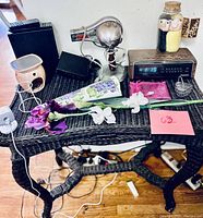 Photo showing black wicker table with items arranged including hand dryer, AM/FM clock, aroma candle burner, silk flowers and twin speakers