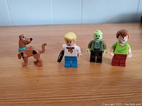 Photo of 4 Lego minifigures from Scooby Doo series: Scooby Doo, Fred, Zombie, Shaggy on wooden surface.