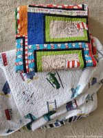 Photograph showing both folded blankets stacked, with the smaller colorful Cat in the Hat blanket on top and the larger white airplane-patterned blanket underneath.