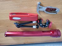 Overview of lot items: large red Maglite flashlight, red Swingline stapler, multi-tool with hammerhead and wooden handle, and small black and red tripod grip holder.