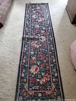 Full view of the narrow Oriental type runner rug laid flat on a light carpeted floor showing the overall floral pattern and border.