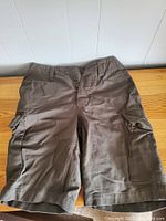 Front view of olive green moleskin cargo shorts with two cargo pockets on legs, button fly, and belt loops.