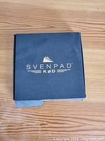 Closed SvenPad branded dark box with gold lettering on wooden surface.